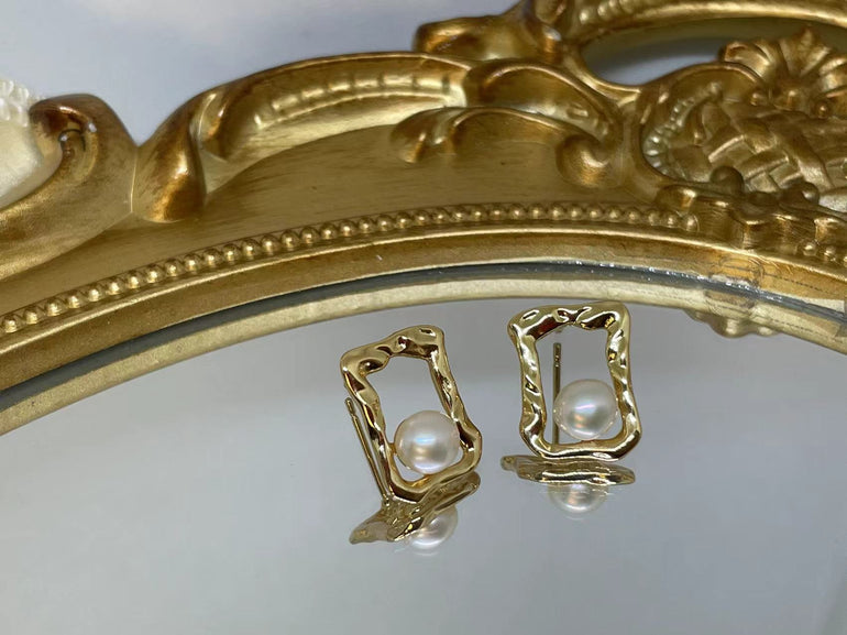 Gold quadrate stud earrings with freshwater pearls, displayed on a mirrored surface.