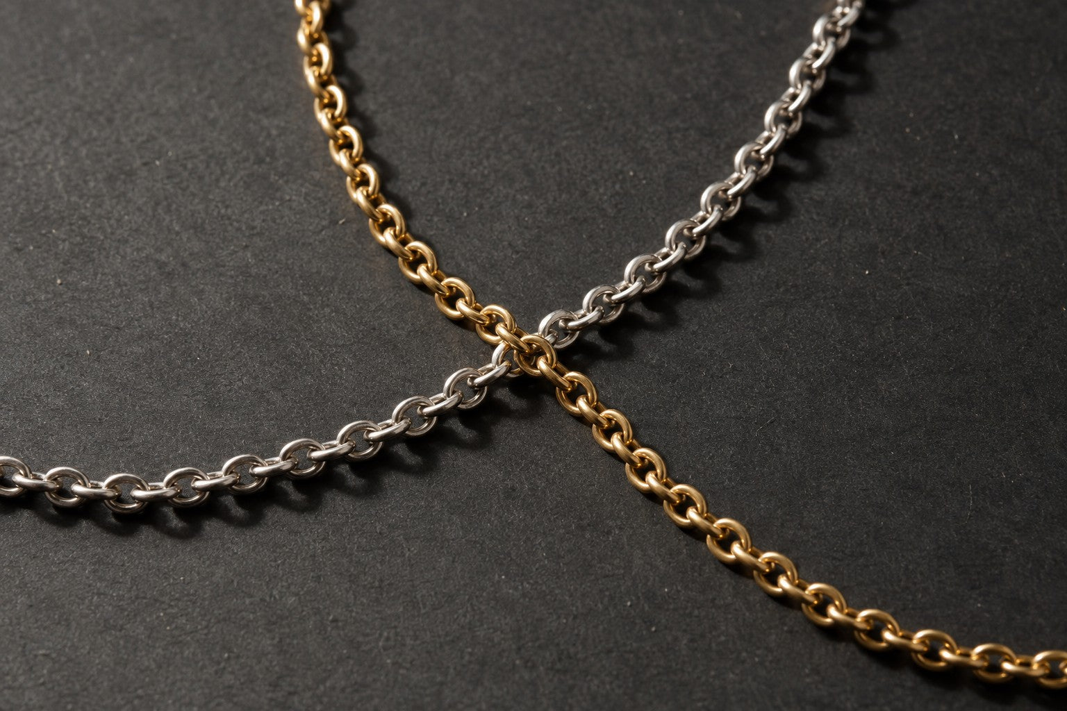 A gold chain and a sterling silver chain crossing on a black background