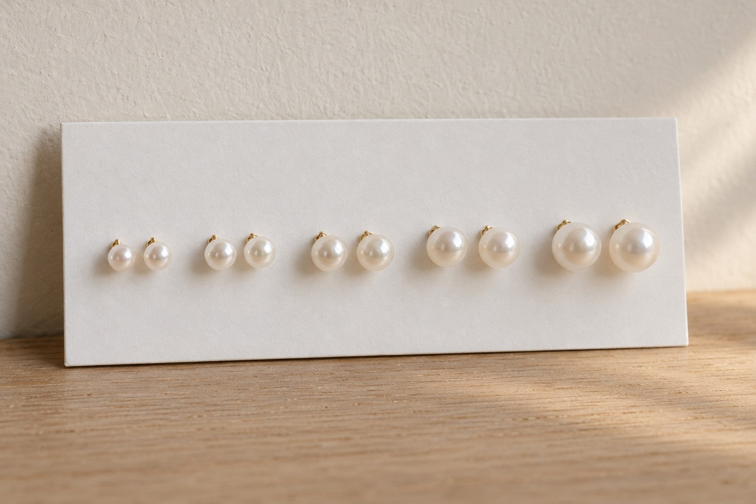 Five pairs of pearl stud earrings from small to large on a white display card