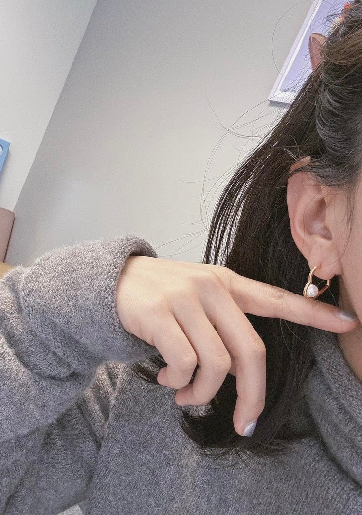 A person wears a gold heart-shaped earring with a freshwater pearl.