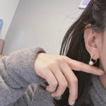 A person wears a gold heart-shaped earring with a freshwater pearl.