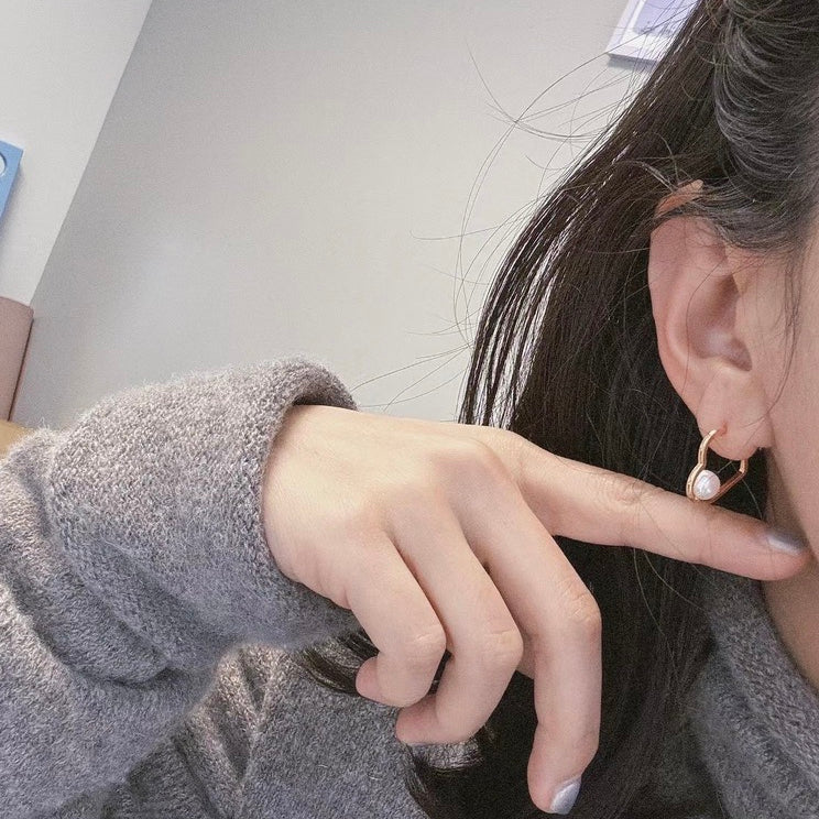 A person wears a gold heart-shaped earring with a freshwater pearl.