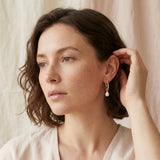 A woman wears Caellia 14K gold twisted hoop earrings with a dangling freshwater pearl.