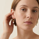 A model wears Caellia 14K gold twisted hoop earrings featuring a dangling freshwater pearl.