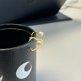 Gold heart-shaped earrings with freshwater pearls resting on a black leather cup.