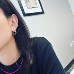 Simple hoop pearl earrings on a woman's ear, with a pink beaded necklace.