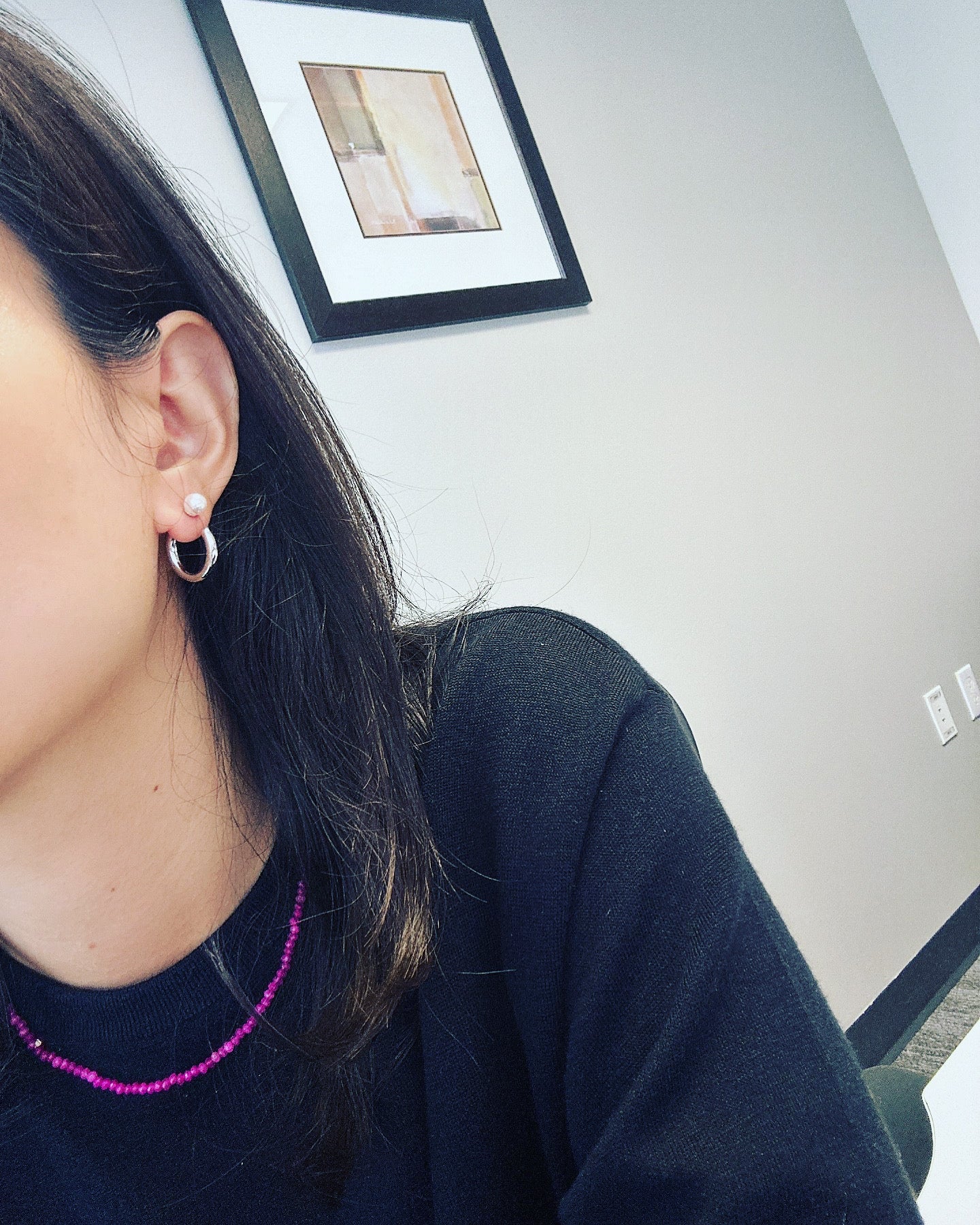 Simple hoop pearl earrings on a woman's ear, with a pink beaded necklace.