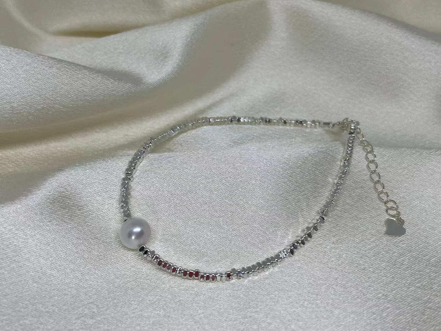 A silver bracelet with a single freshwater pearl and a section of red beads.