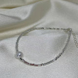 A silver bracelet with a single freshwater pearl and a section of red beads.