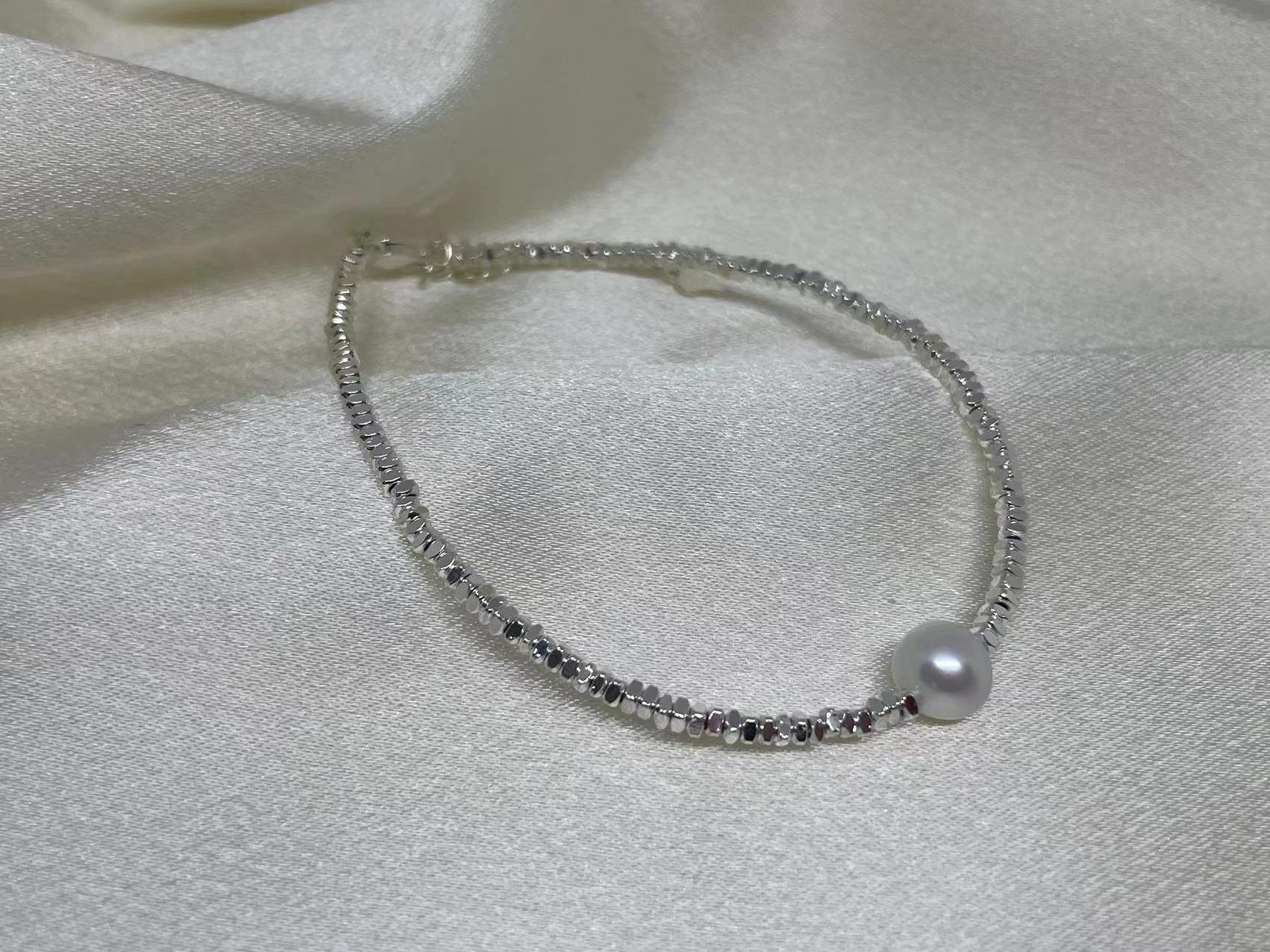 A silver bracelet with small faceted beads and a single freshwater pearl.