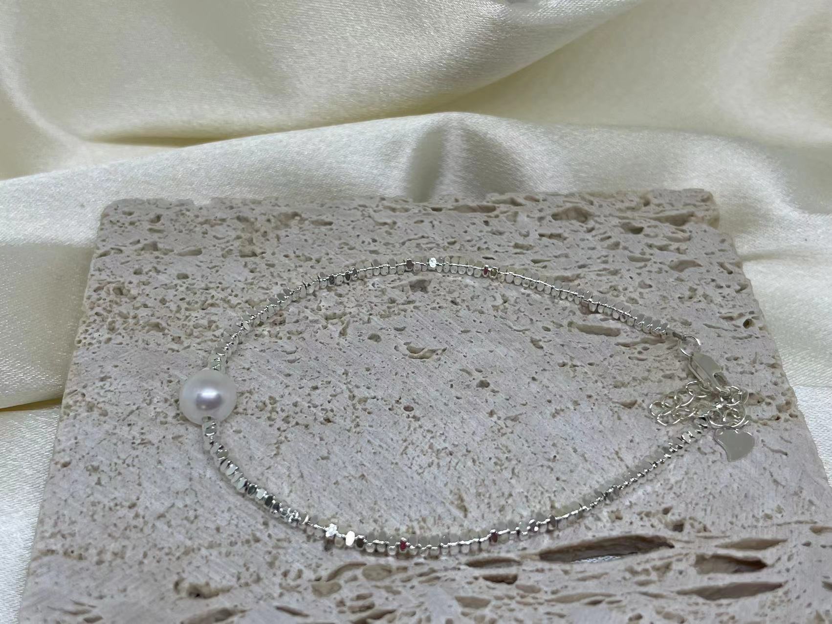 A silver bracelet with a single freshwater pearl on a textured stone surface.