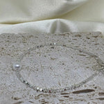 A silver bracelet with a single freshwater pearl on a textured stone surface.