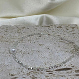 A silver bracelet with a single freshwater pearl on a textured stone surface.