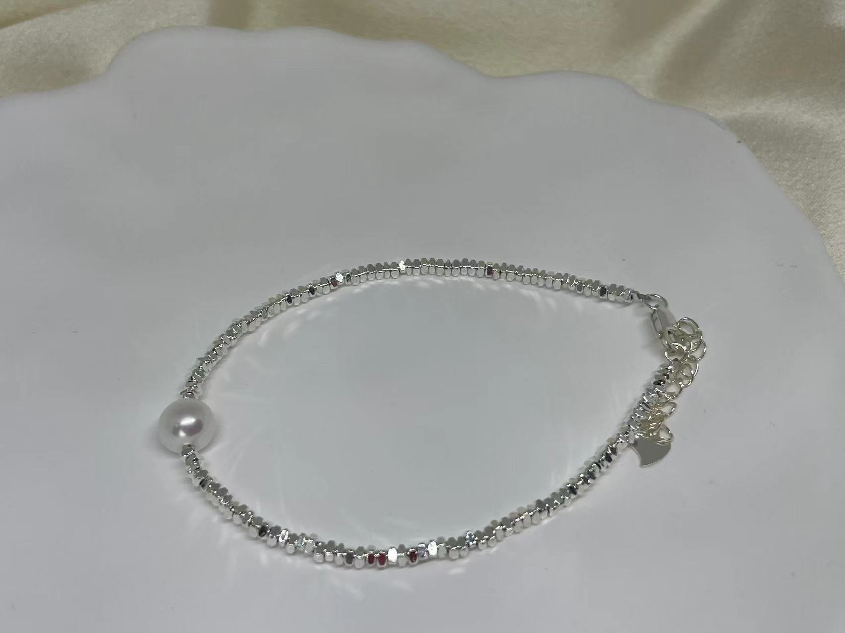 A silver beaded bracelet with a single freshwater pearl and a heart charm.