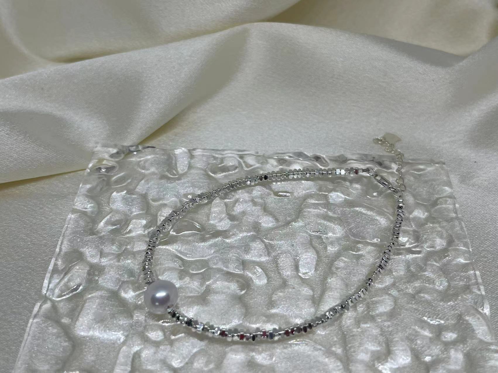 Freshwater pearl silver bracelet on a clear textured surface with a white fabric background.