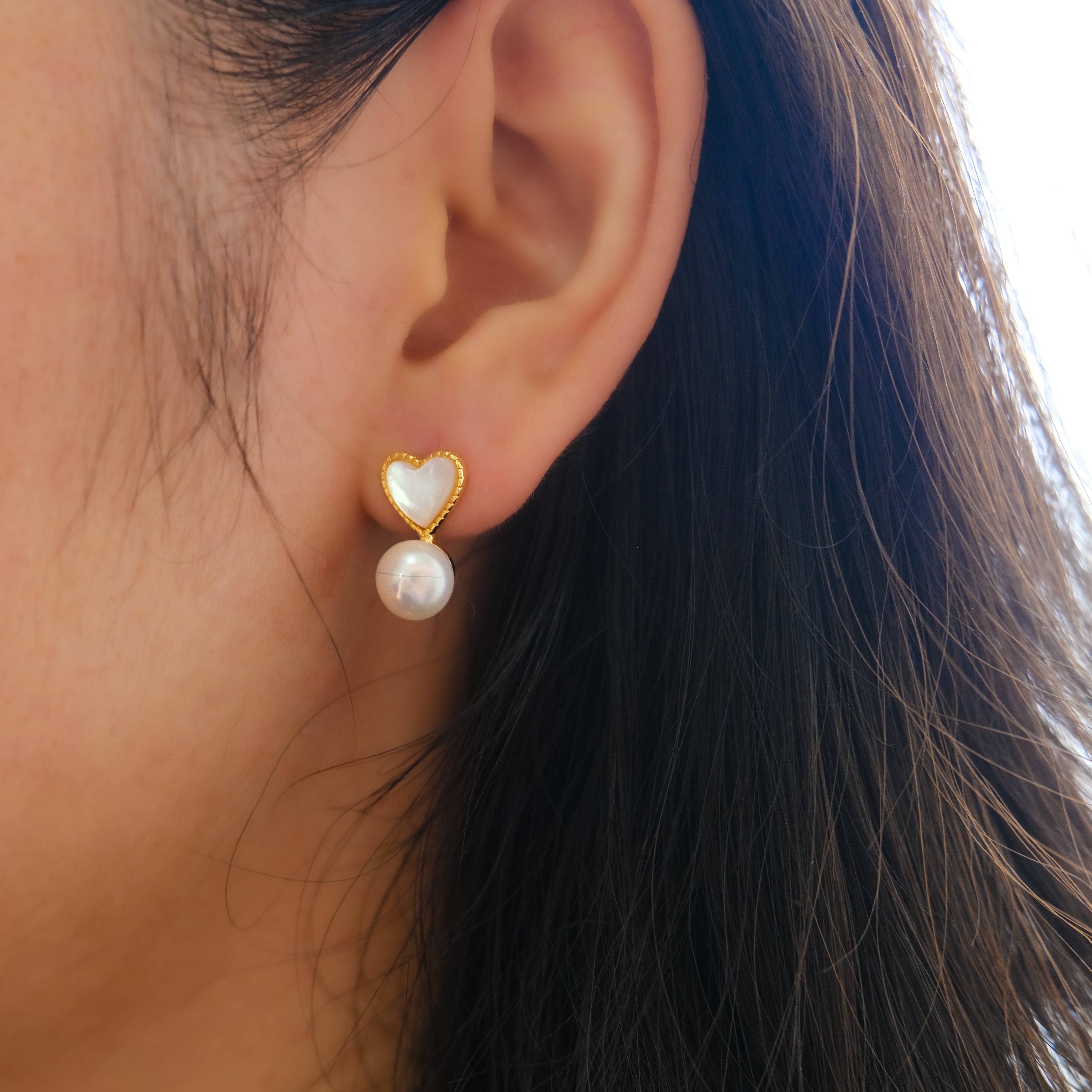 A close-up of a person wearing a heart-shaped pearl stud earring.
