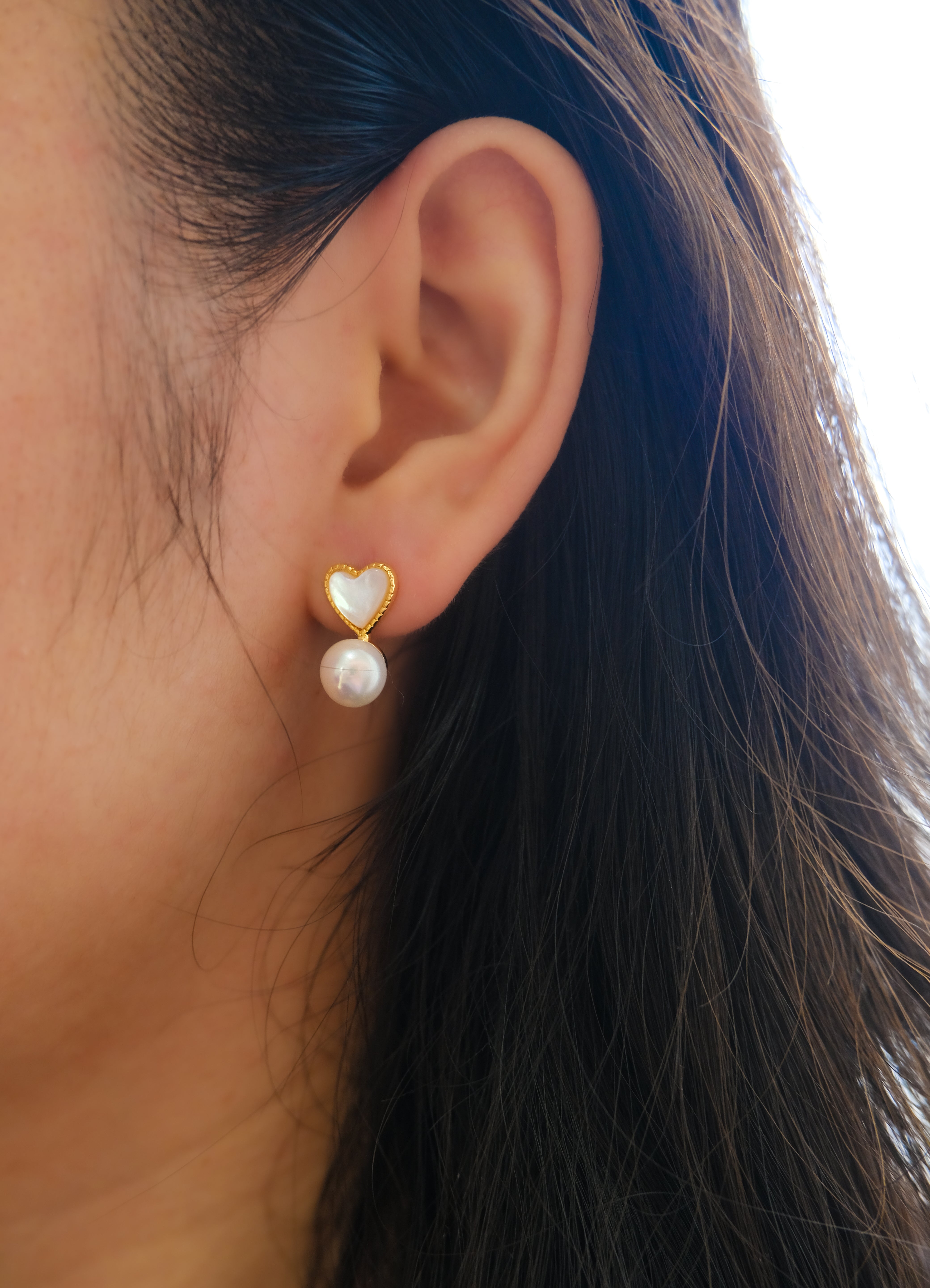 A close-up of a person wearing a heart-shaped pearl stud earring.
