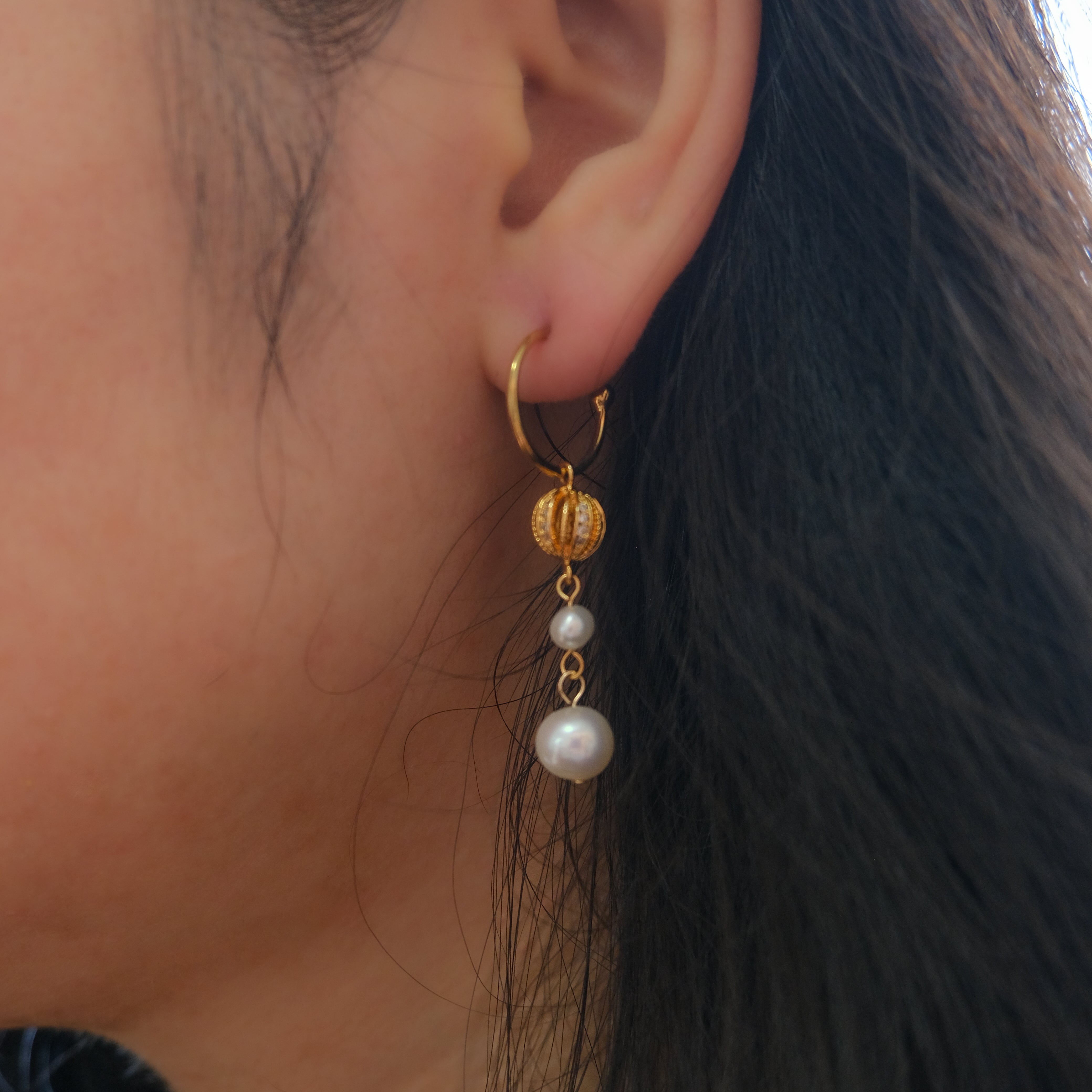 A gold hoop earring with a pumpkin-shaped charm and two dangling pearls.