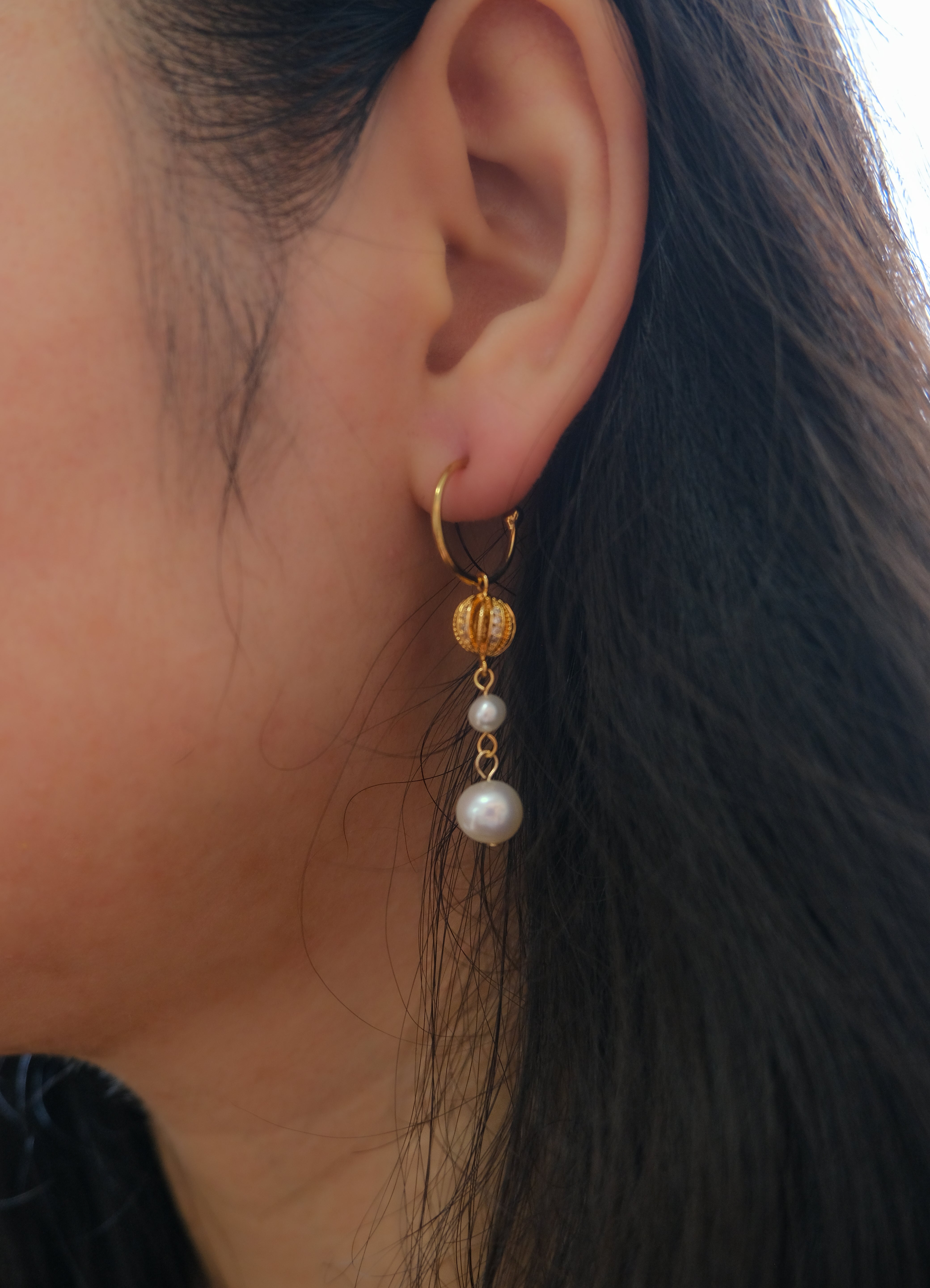 A gold hoop earring with a pumpkin-shaped charm and two dangling pearls.