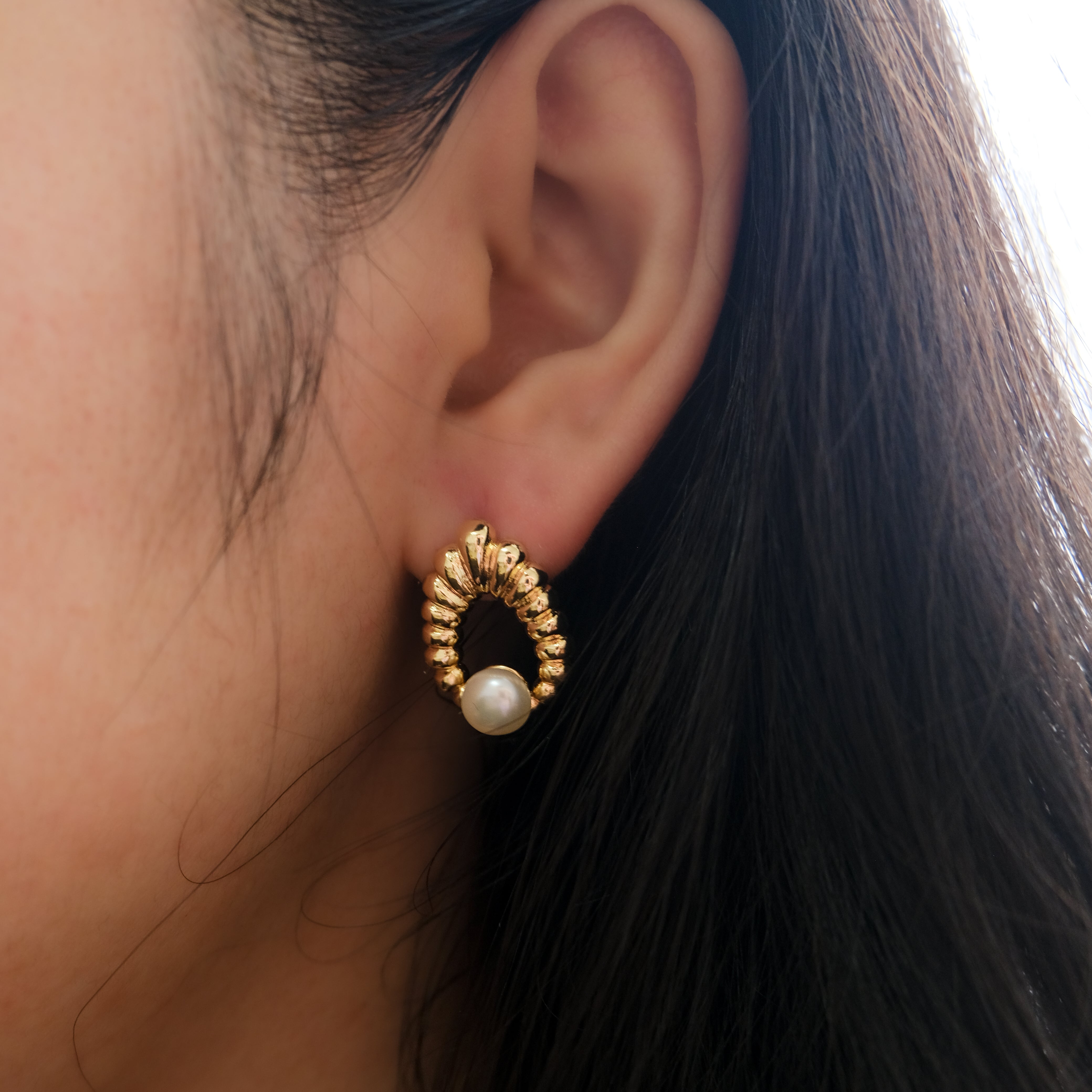 A gold water drop shaped earring with a freshwater pearl on a woman's ear.
