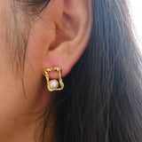 A gold quadrate stud earring with a freshwater pearl on a person's ear.
