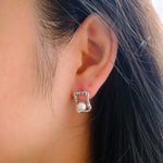 A silver quadrate stud earring with a freshwater pearl on a person's ear.