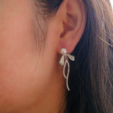 Elegant pearl bow dangle earrings with a silver-plated chain on a woman's ear.