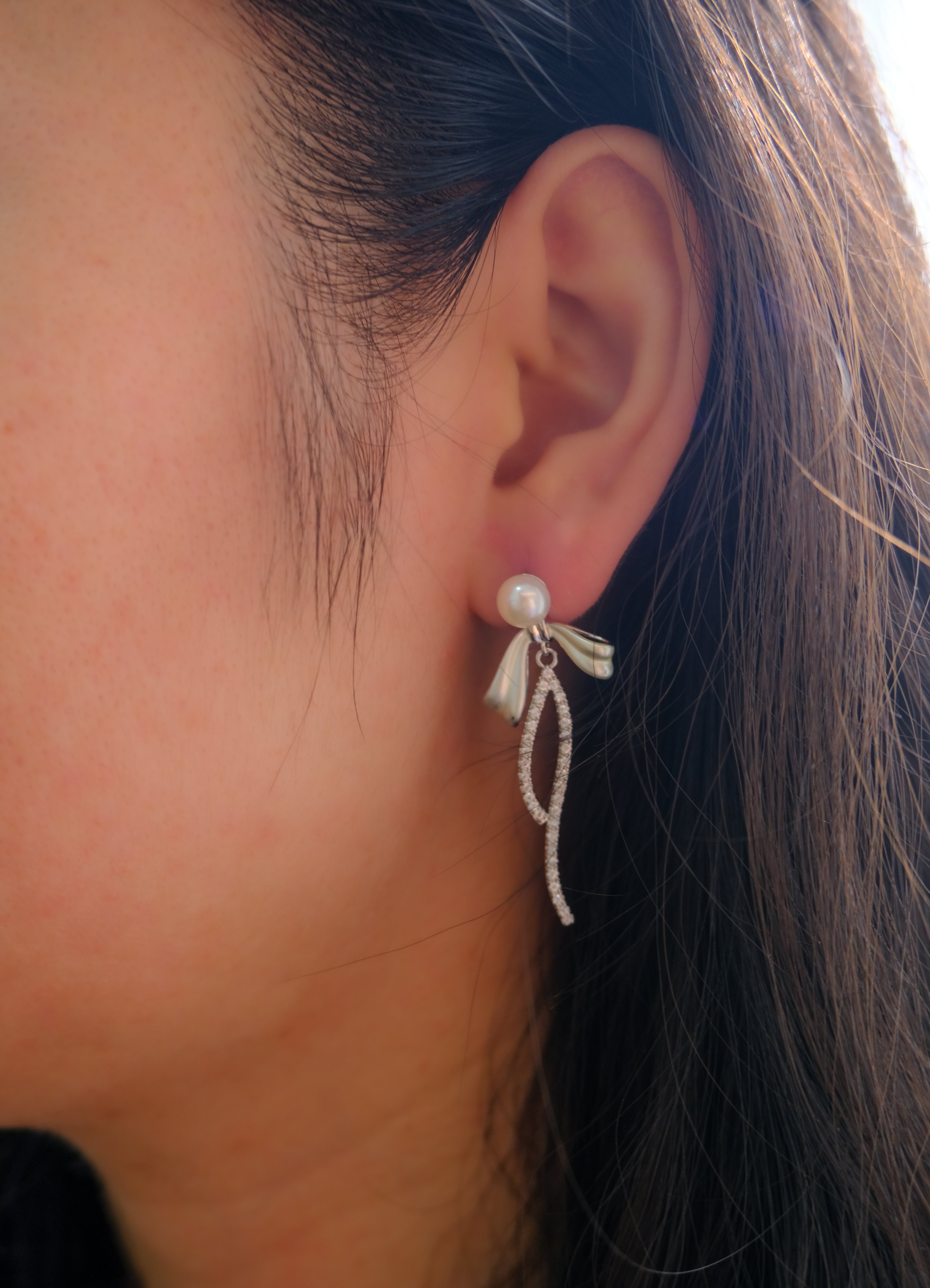 Elegant pearl bow dangle earrings with a silver-plated chain on a woman's ear.