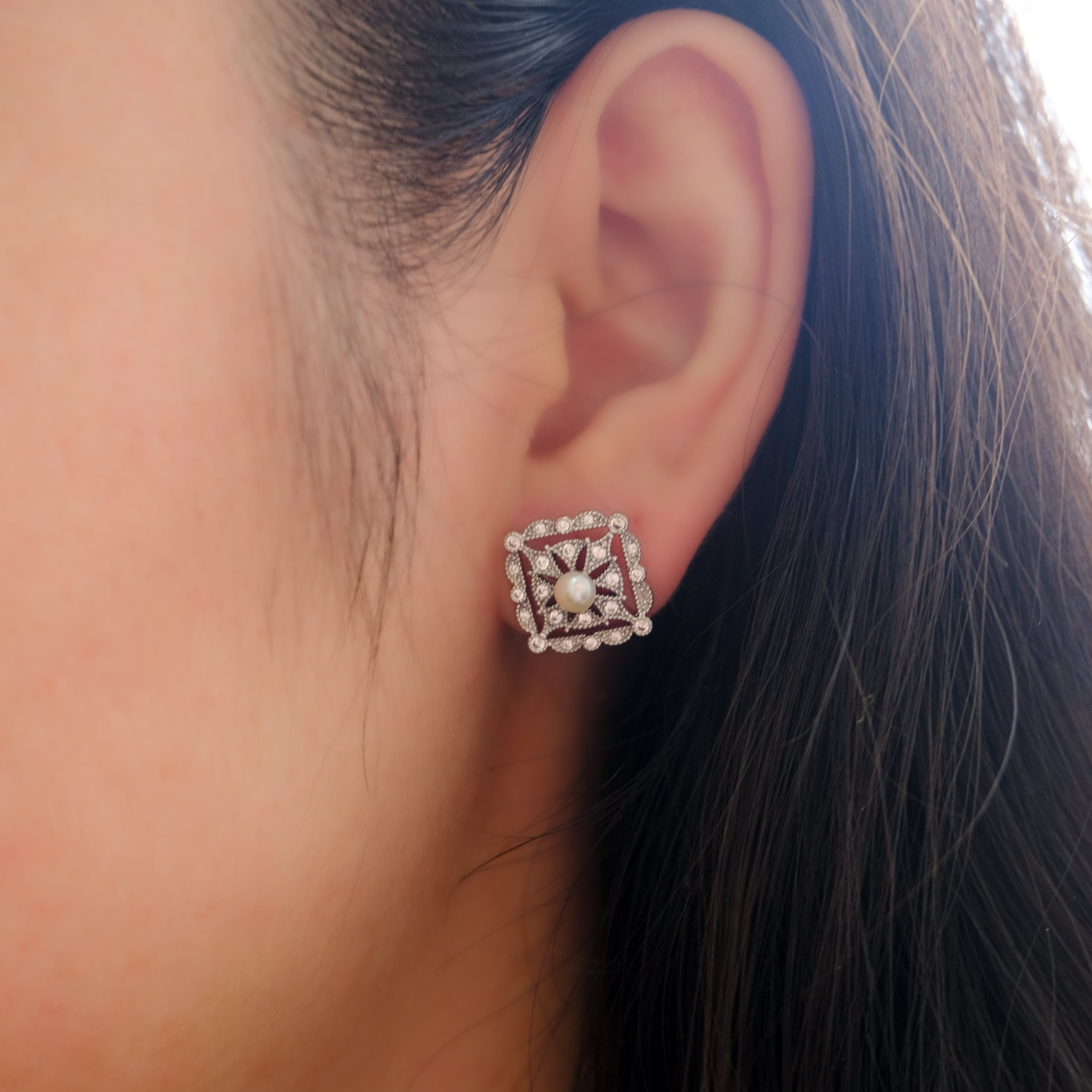 A woman wears a silver quadrate stud earring with a pearl and diamonds.