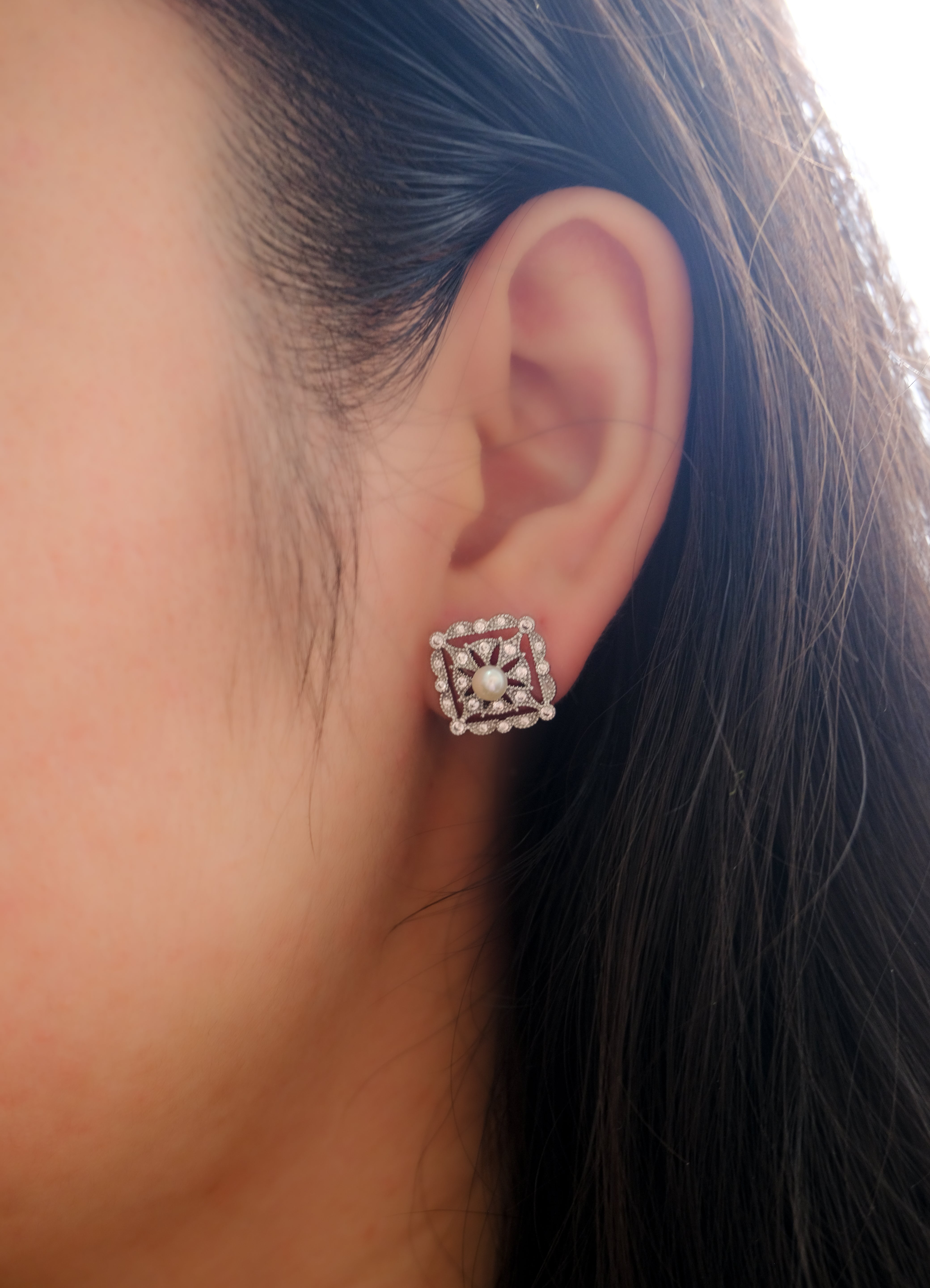 A woman wears a silver quadrate stud earring with a pearl and diamonds.