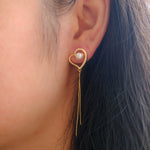 A gold heart-shaped earring with a pearl and dangling chains on a woman's ear.