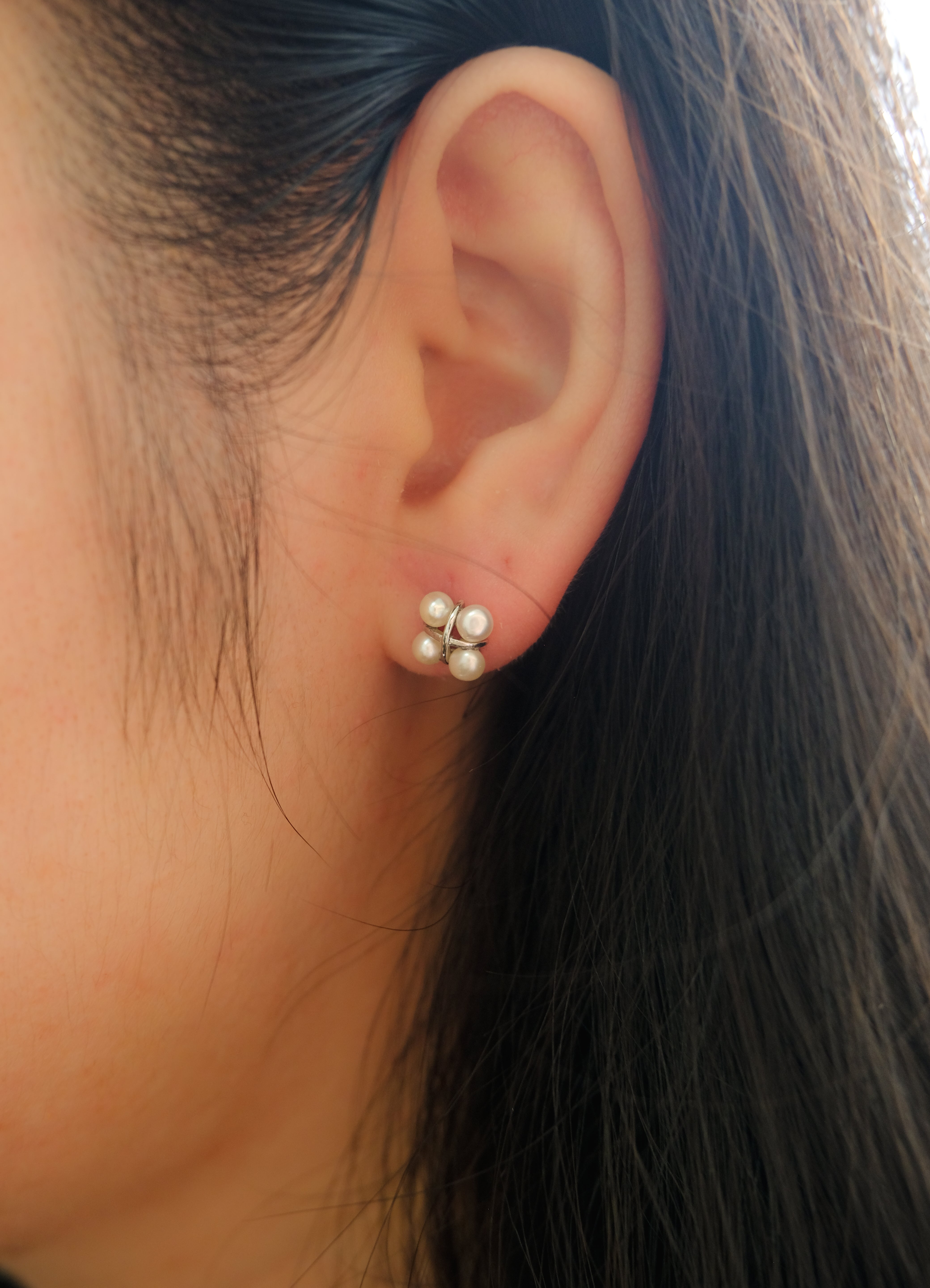 A close-up of a woman's ear wearing a four freshwater pearl rhomboid stud earring.