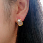 A close-up of a woman's ear wearing a gold earring with a pearl and a white stone.