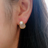 A close-up of a woman's ear wearing a gold earring with a pearl and a white stone.