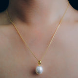 A gold chain necklace with a large, off-round white freshwater pearl pendant.