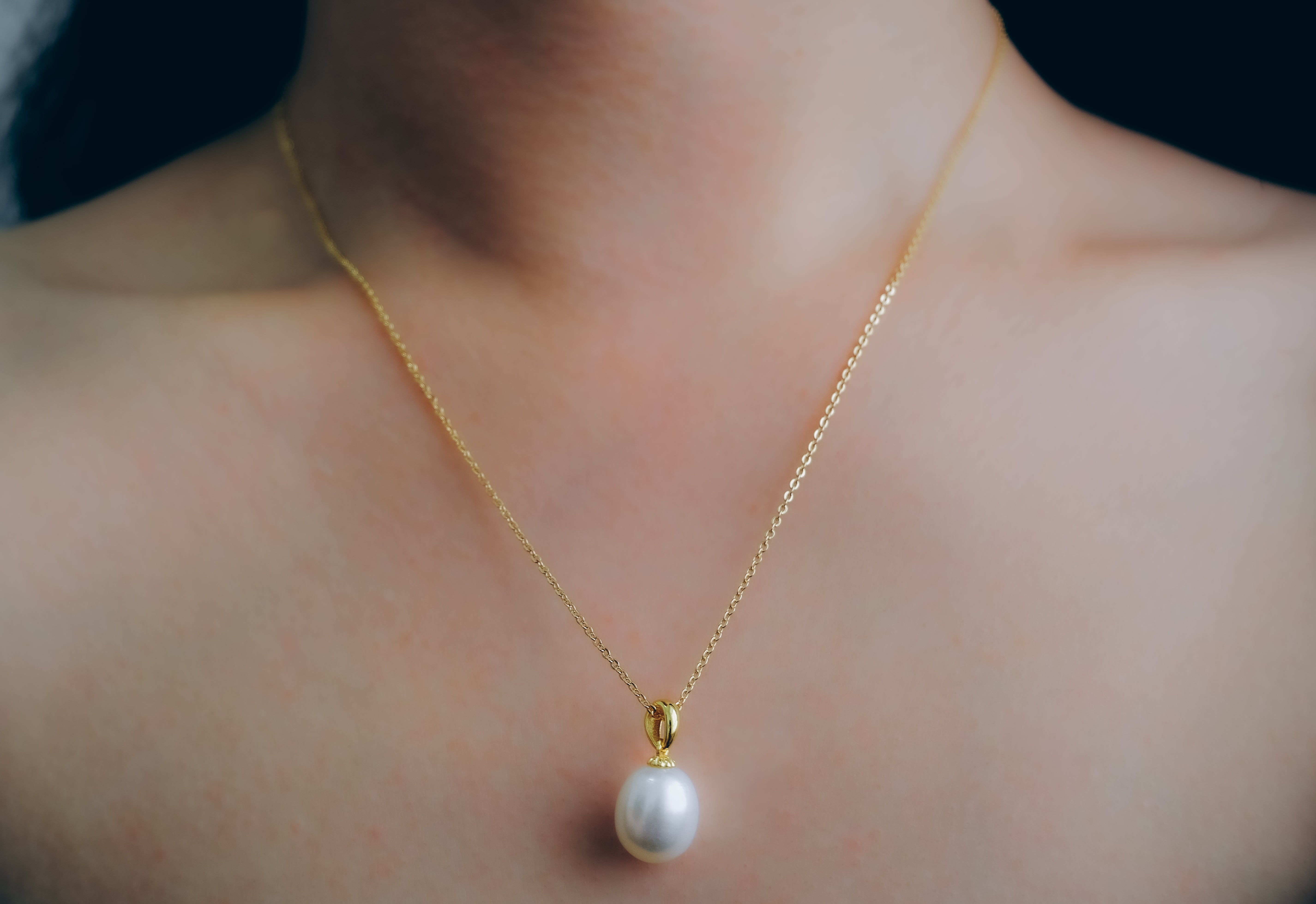 A gold chain necklace with a large, off-round white freshwater pearl pendant.