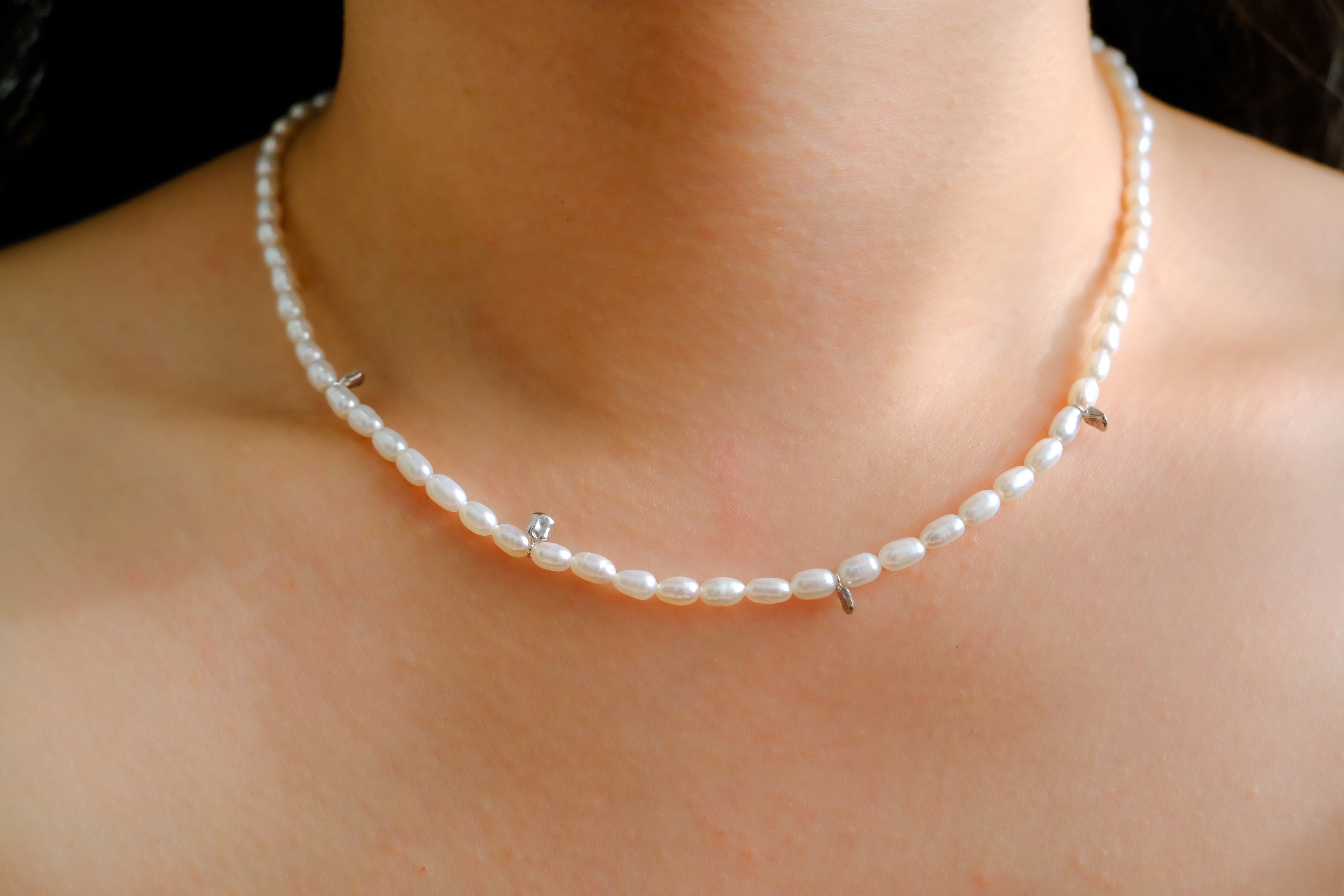 A woman wears a single strand of off-round freshwater pearls with silver accents.