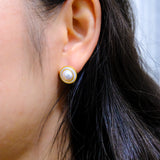 A woman wears a round freshwater pearl earring with a gold-plated frame.