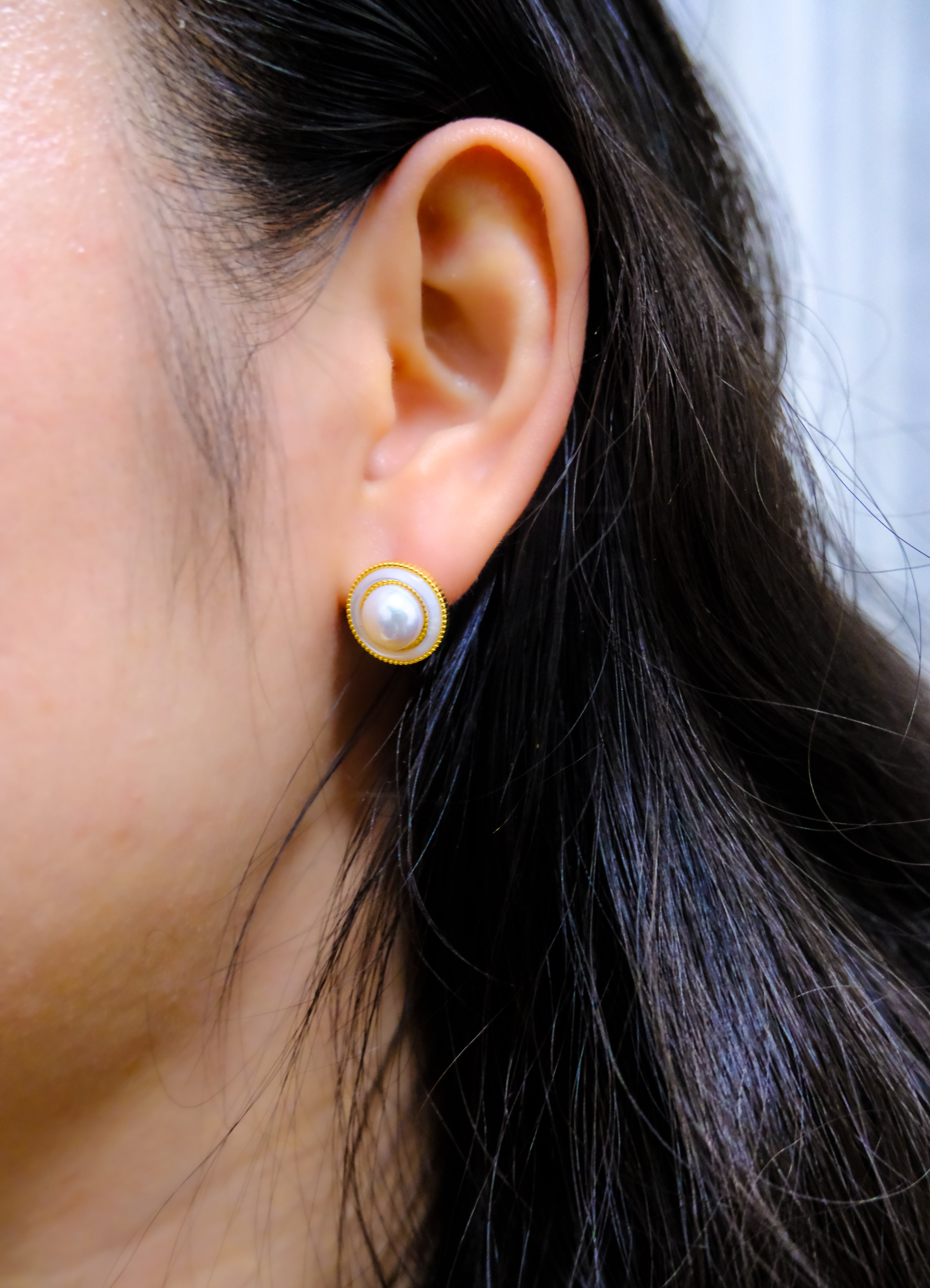 A woman wears a round freshwater pearl earring with a gold-plated frame.