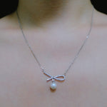 A silver chain necklace with a dainty bow pendant and a single freshwater pearl.