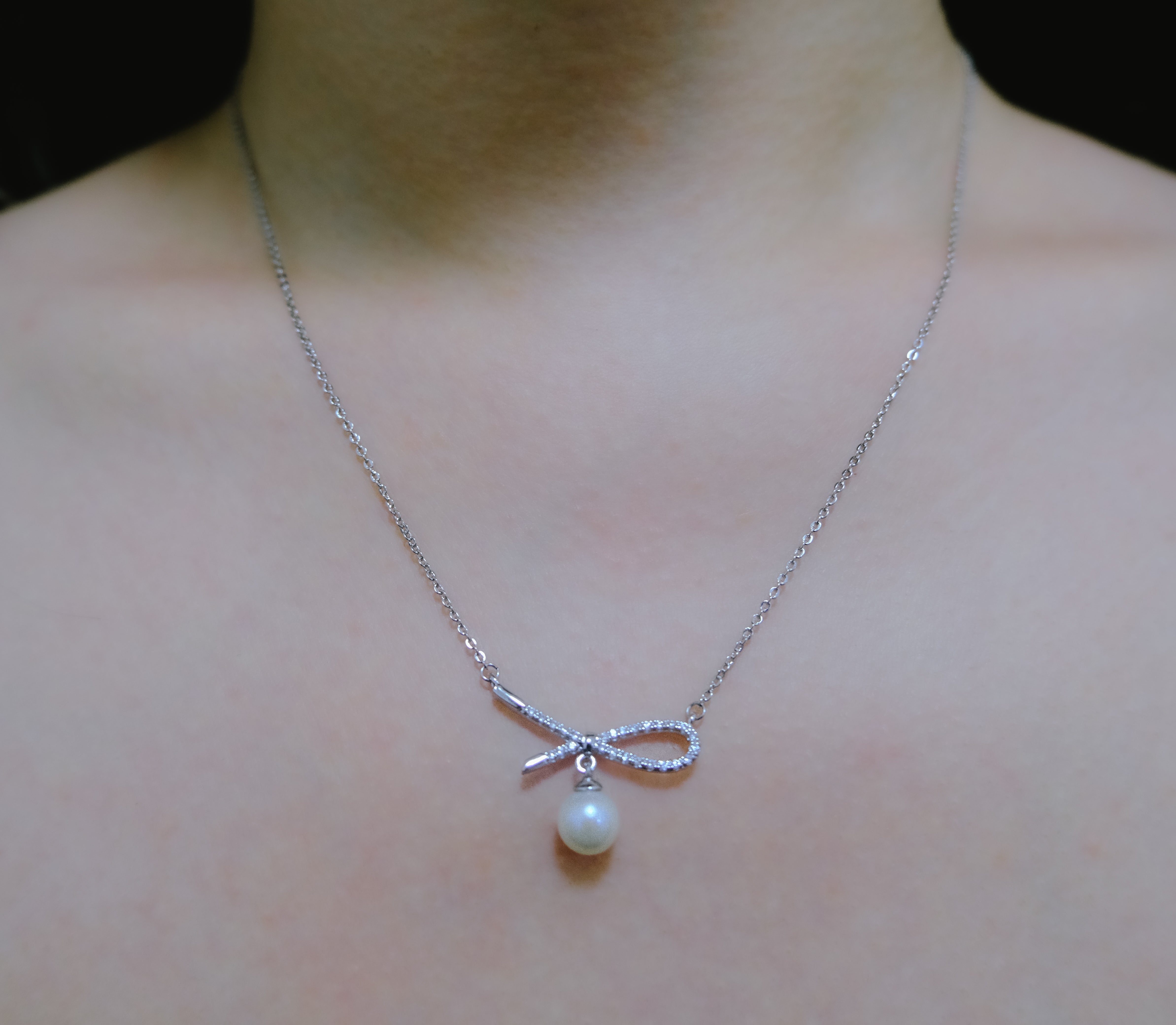 A silver chain necklace with a dainty bow pendant and a single freshwater pearl.