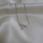 A silver necklace with a bow-shaped pendant and a single freshwater pearl.
