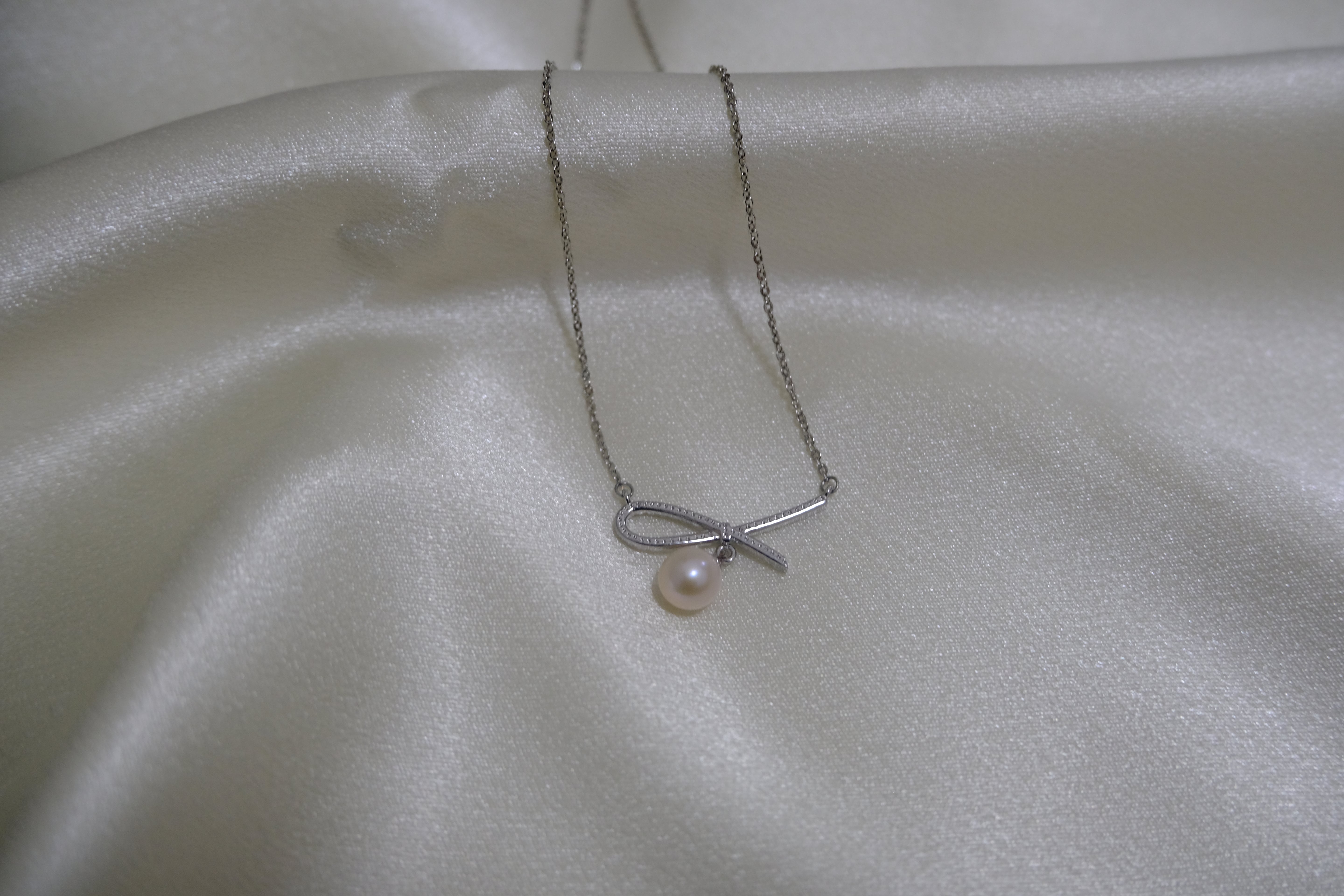 A silver necklace with a bow-shaped pendant and a single freshwater pearl.