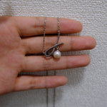 A silver bow pendant with a freshwater pearl hangs from a delicate chain on a hand.