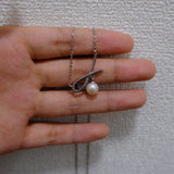 A silver bow pendant with a freshwater pearl hangs from a delicate chain on a hand.