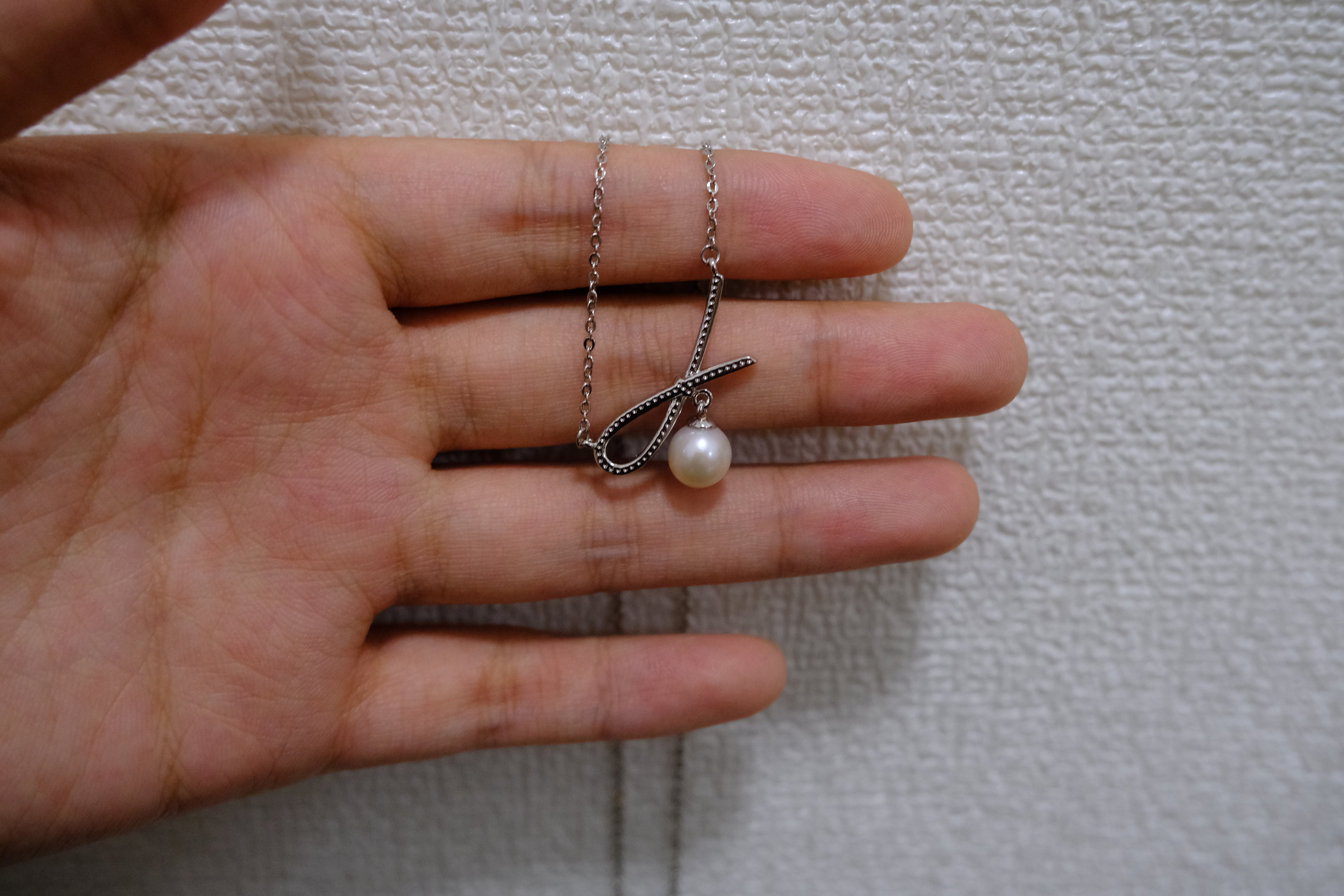 A silver bow pendant with a freshwater pearl hangs from a delicate chain on a hand.