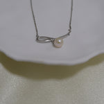 A silver chain necklace with a bow-shaped pendant holding a single pearl.