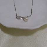 A silver chain necklace with a bow-shaped pendant holding a single pearl.