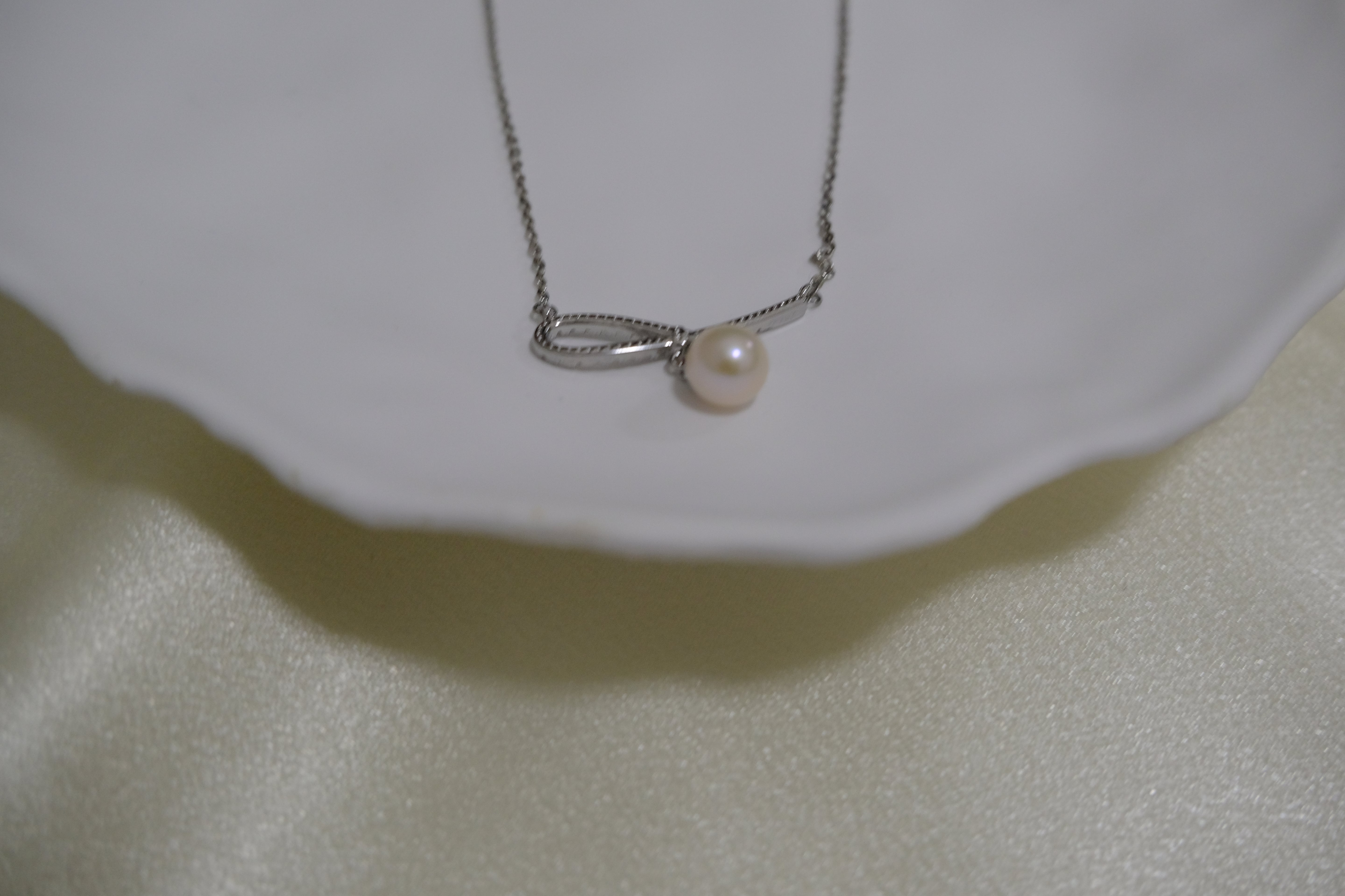 A silver chain necklace with a bow-shaped pendant holding a single pearl.