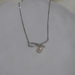 A silver chain necklace with a bow-shaped pendant and a single freshwater pearl.